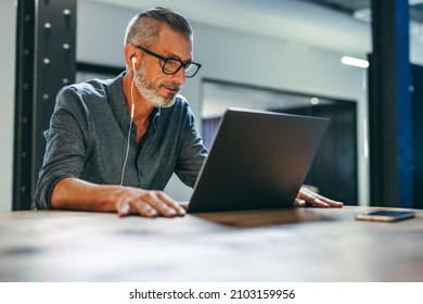 Businessman Attending A Virtual Meeting In A Modern Office. Experienced Entrepreneur Using A Laptop For A Video Conference With His Partners. Mature Businessman Sitting In A Boardroom.