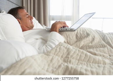 Businessman In Bathrobe Working With Laptop On Hotel Bed Drinking Coffee