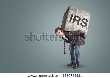 Businessman bending under a heavy stone with the letters IRS printed on it - tax office concept
