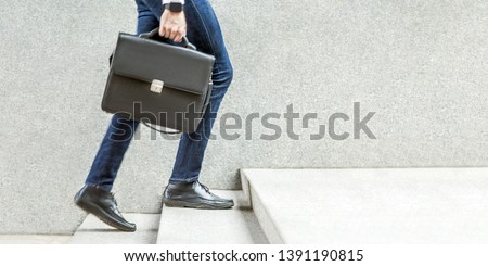 Businessman with black briefcase in hand walking up on stairs. business goal, improvement, progress, Increase and growth concept. Outdoor closeup shot. in grey wall copy space.