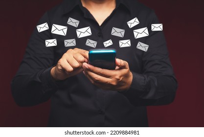 A Businessman In A Black Shirt Holding A Smartphone Receives A New Message With Email Icons While Standing In The Office. Email Notification On A Mobile Phone. Email Marketing Concept. Close-up Photo