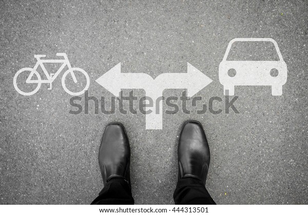 Businessman in black shoes standing at the crossroad\
making decision what transportation vehicle to use - bicycle or\
car