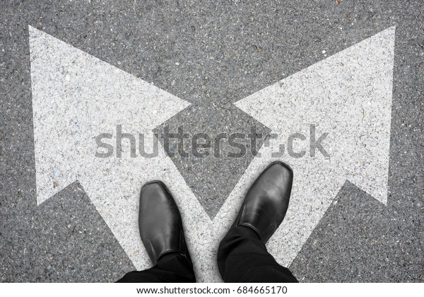 Businessman in black\
shoes standing at the crossroad making decision which way to go.\
Decision making\
concept.