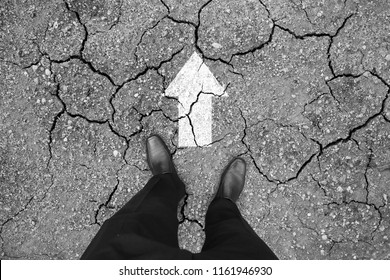 Businessman In Black Shoes Standing On Cracked Dry Floor With Direction To Go Forward. Business Hardship And Difficulty Concept.