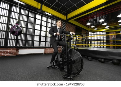 Businessman In A Black Suit Is Engaged On An Exercise Bike In A Boxing Club.