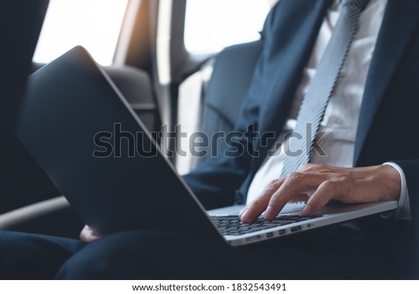 Businessman in black\
suit, executive manager working on laptop computer inside a car on\
backseat, portable office, business concept. Corporate man going to\
workplace by taxi, close\
up