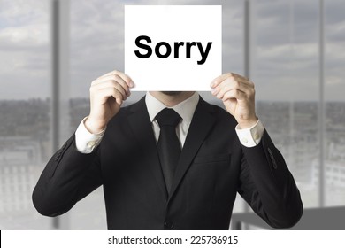 Businessman In Black Suit Hiding Face Behind Sign Sorry