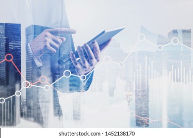 Businessman in black suit using tablet computer with double exposure of cityscape and graphs. Concept of stock market and trading. Toned image - Shutterstock ID 1452138170
