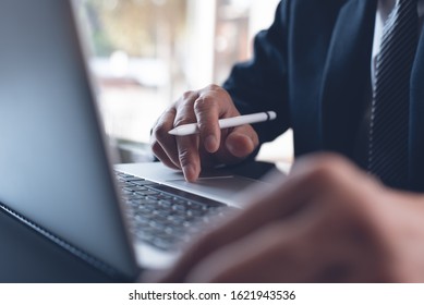 Businessman In Black Suit Working In Modern Office. Business Man Hand With Stylus Pen Typing And Networking On Laptop Computer, Reviewing Marketing Report On Table, Close Up