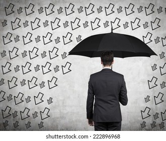 Businessman With Black Umbrella Standing Under The Drawn Storm Of Arrows. Photo Over Concrete Background. A Concept Of Risk Avoidance. 