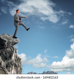 Businessman in a blindfold stepping off a cliff ledge concept for risk, challenge, conquering adversity or ignorance