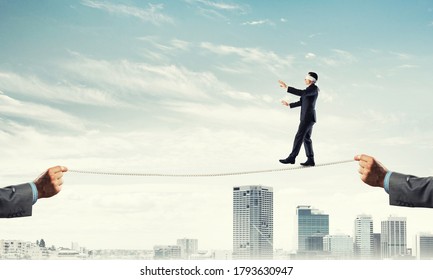 Businessman with blindfolder on eyes walking on rope over cityscape background