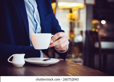 Businessman in a blue jacket with a cup of coffee in the cafe at the table, close-up