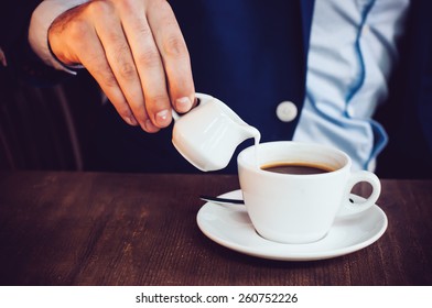 Businessman in blue jacket pours cream into coffee in a cafe at the table, close-up - Powered by Shutterstock