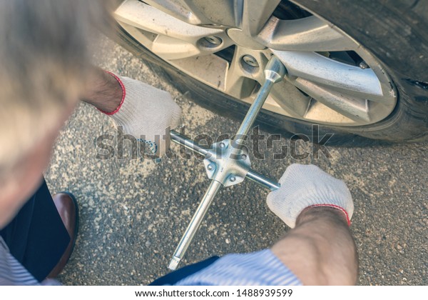 A\
businessman in a blue suit using cross wrench tighten the bolts\
wheel of punctured wheel. Hole in the tire.\
Concept