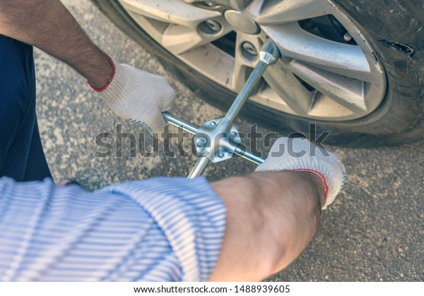 A\
businessman in a blue suit using cross wrench tighten the bolts\
wheel of punctured wheel. Hole in the tire.\
Concept