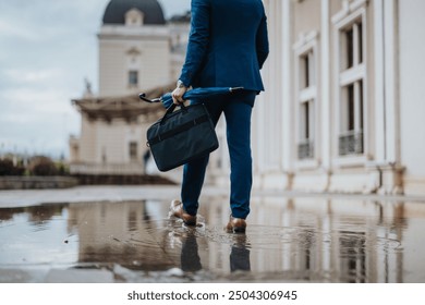 Businessman in a blue suit walking on a rainy day with a briefcase and umbrella near an office building. Reflections in puddles create a professional and determined mood. - Powered by Shutterstock