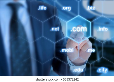 Businessman in blue touching the domain ending com on a hexagon grid in front of office background - Shutterstock ID 533372242
