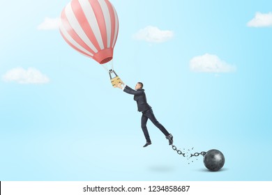A businessman breaks away from a chain and iron ball to catch a small hot air balloon. Touching your dream. Breaking free for adventure. Business and personal achievement.