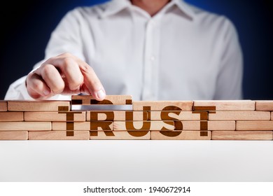 Businessman builds a structure of wooden blocks with the word trust. Building trust in business concept.