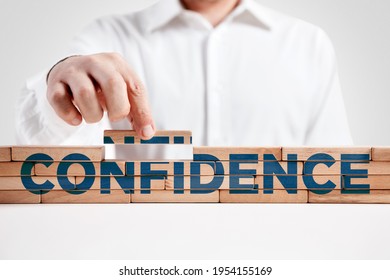 Businessman Builds A Structure Of Wooden Blocks With The Word Confidence. Building Confidence Concept.