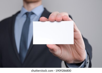 Businessman ,Business Man's Hand Hold Showing Business Card - Close Up Shot On Grey Background. Show A Blank Piece Of Paper. Paper Visit Card.