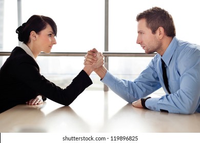 Businessman and businesswoman arm wrestling on desk in office