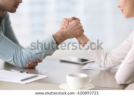 Businessman and businesswoman armwrestling at the office table, maintaining eye contact, trying to get leadership, fighting for equal rights for women, business competitors in the marketplace