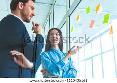 The businessman and a businesswoman discussing near the glass with a graph