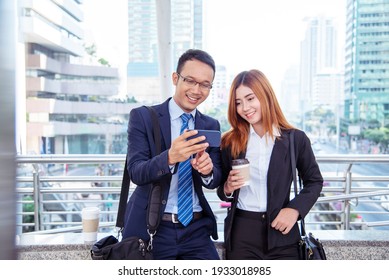 Businessman Businesswoman Drinking Coffee In Town Using Smartphone Outside Office Modern City. Hands Holding Take Away Coffee Cup And Smart Phone Talking Together Business Partner With Cup Of Coffee