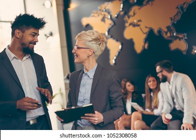 Businessman And Businesswoman Reviewing Contract; Business Team Working In The Background. Focus On The Man In The Foreground