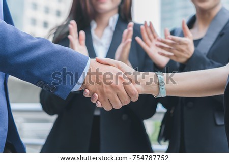 Businessman and businesswoman shaking hand and smiling after discuss new project success, supported by colleagues applauded in cityscape background, business people conceptbusiness concept