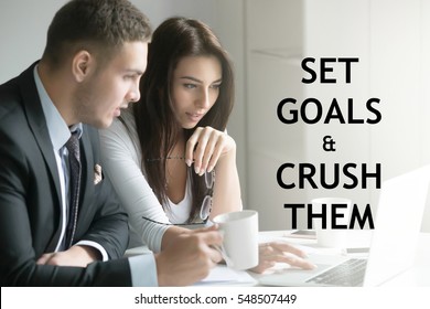 Businessman and businesswoman sitting at office desk, office workers looking at the laptop, discussing business ideas. Photo with motivational text "Set goals and crush them". Business concept photo