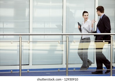 Businessman and businesswoman walking and talking on modern office building corridor. - Powered by Shutterstock