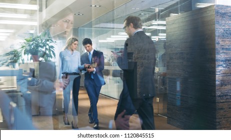 Businessman and Businesswoman Walking Through Glass Hallway, Discussing Work and Using Tablet Computer. Busy Corporate Office Building with Many Workers.