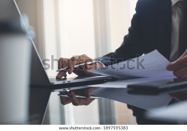 Businessman busy  working on\
laptop computer with mobile smart phone on table at modern office.\
Business man reviewing business document. consultant lawyer\
concept