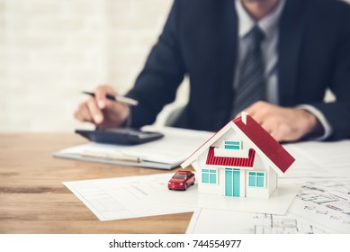 Businessman calculating budget before signing real estate project contract with house and car model at the table in the office