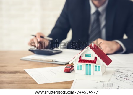 Businessman calculating budget before signing real estate project contract with house and car model at the table in the office