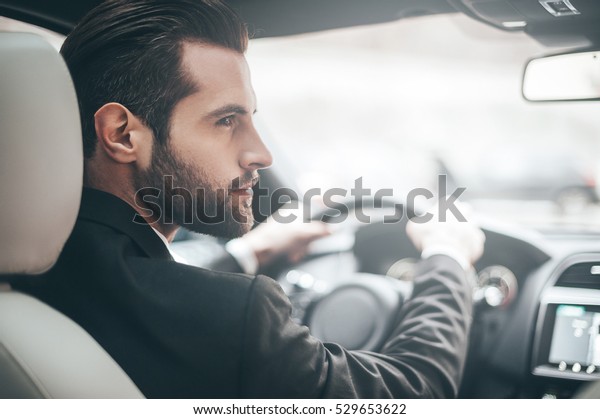 Businessman in car. Rear view of young\
handsome man looking on the right while driving a car\
