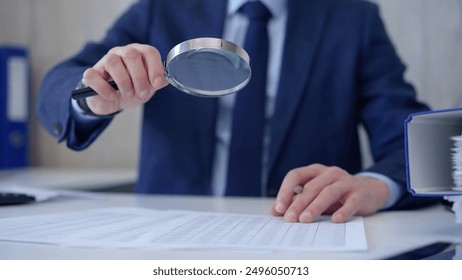 Businessman is carefully examining financial documents with a magnifying glass, highlighting the importance of thorough analysis in business. Audit and taxes. - Powered by Shutterstock