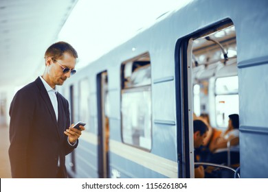 Businessman Checking His Phone Before Getting On Subway. Elegant Man Wearing Formal Clothes For Business Meeting Standing In Front Of Metro Train Texting Via His Phone.