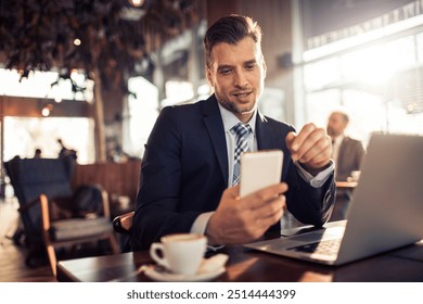 Businessman checking smartphone while working on laptop in a cafe - Powered by Shutterstock