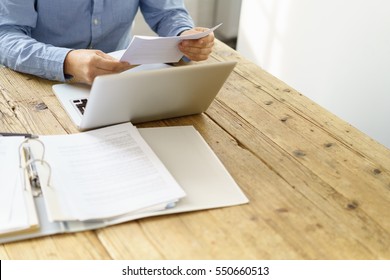 Businessman checking a typed report or document as he sits working on paperwork at a laptop computer, close up of his hands - Powered by Shutterstock