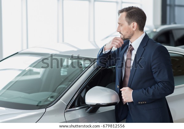 Businessman choosing a car at the dealership\
salon looking at the vehicle thoughtfully rubbing his chin\
copyspace choice buying cars sales offer thinking decision deciding\
automotive transport\
concept