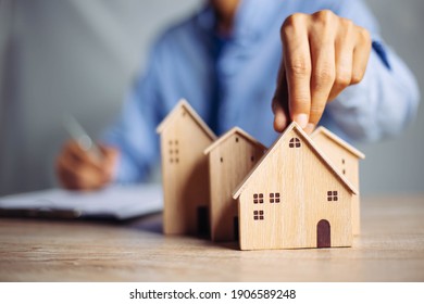 Businessman choosing mini wood house model from model on wood table, Planning to buy property. concept of Choose the best.