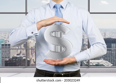 Businessman In A City Office Holding A Silver Dollar Sign, City View Background. 