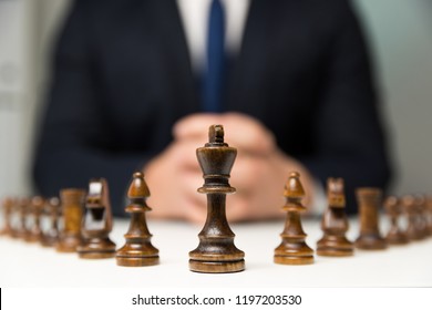 Businessman with clasped hands planning strategy with chess figures on table. Strategy, leadership and teamwork concept.
