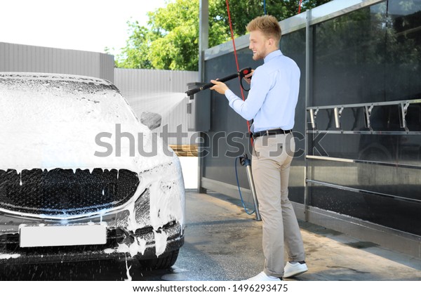 Businessman cleaning auto with high pressure water\
jet at self-service car\
wash
