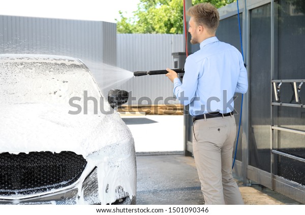 Businessman cleaning auto with high pressure water\
jet at self-service car\
wash
