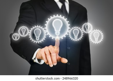 Businessman clicking on a virtual touchscreen with gears with light bulb - Shutterstock ID 248966320
